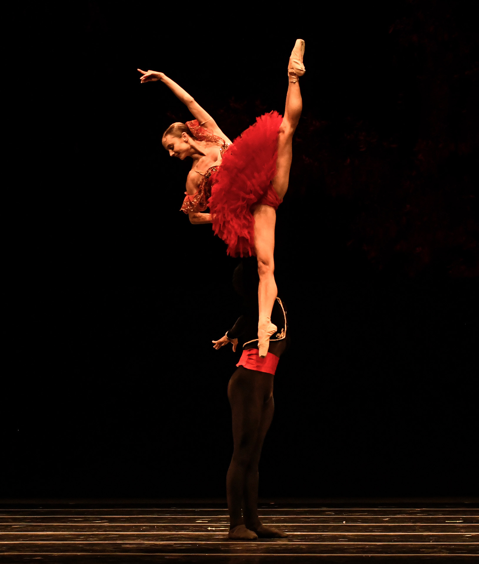 Kotchetkova is lifted by another male dancer. She is wearing a red tutu. 