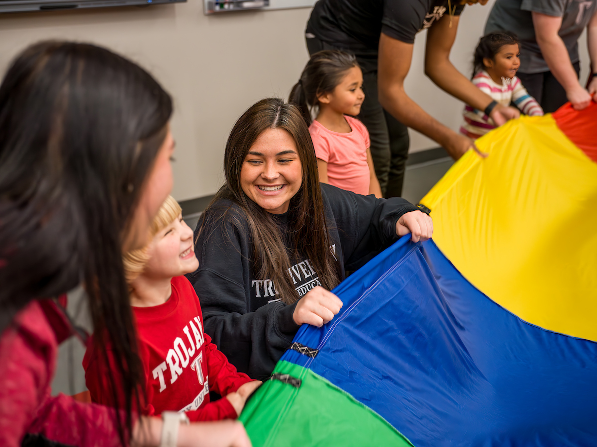 Physical Education student guiding younger children on a physical activity while smiling and having fun. 