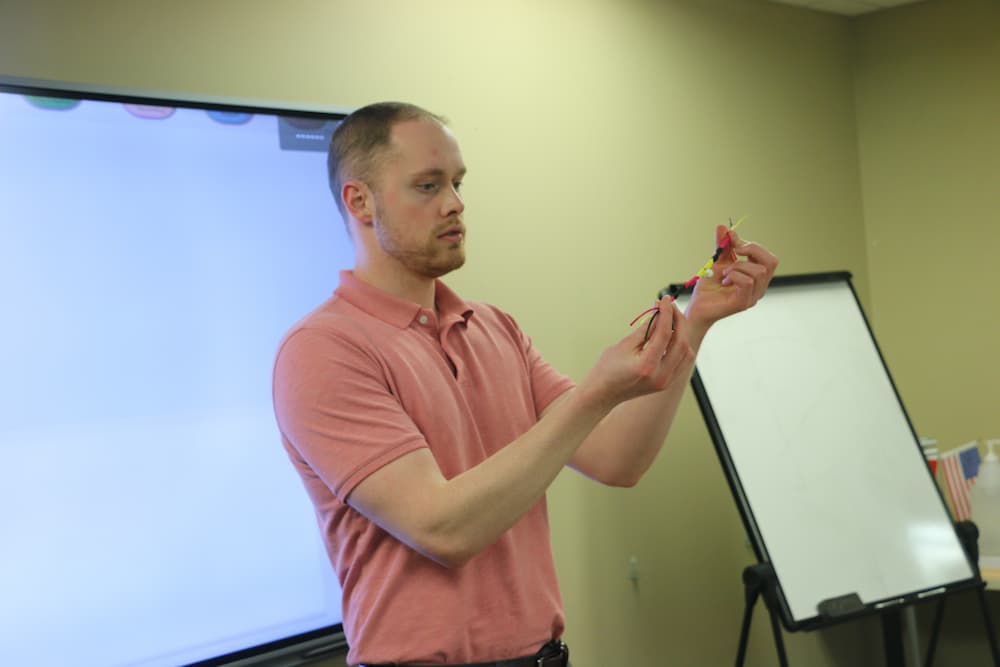 Associate Director Austin Deal showing how to perform one of the more difficult steps in the bracelet making process