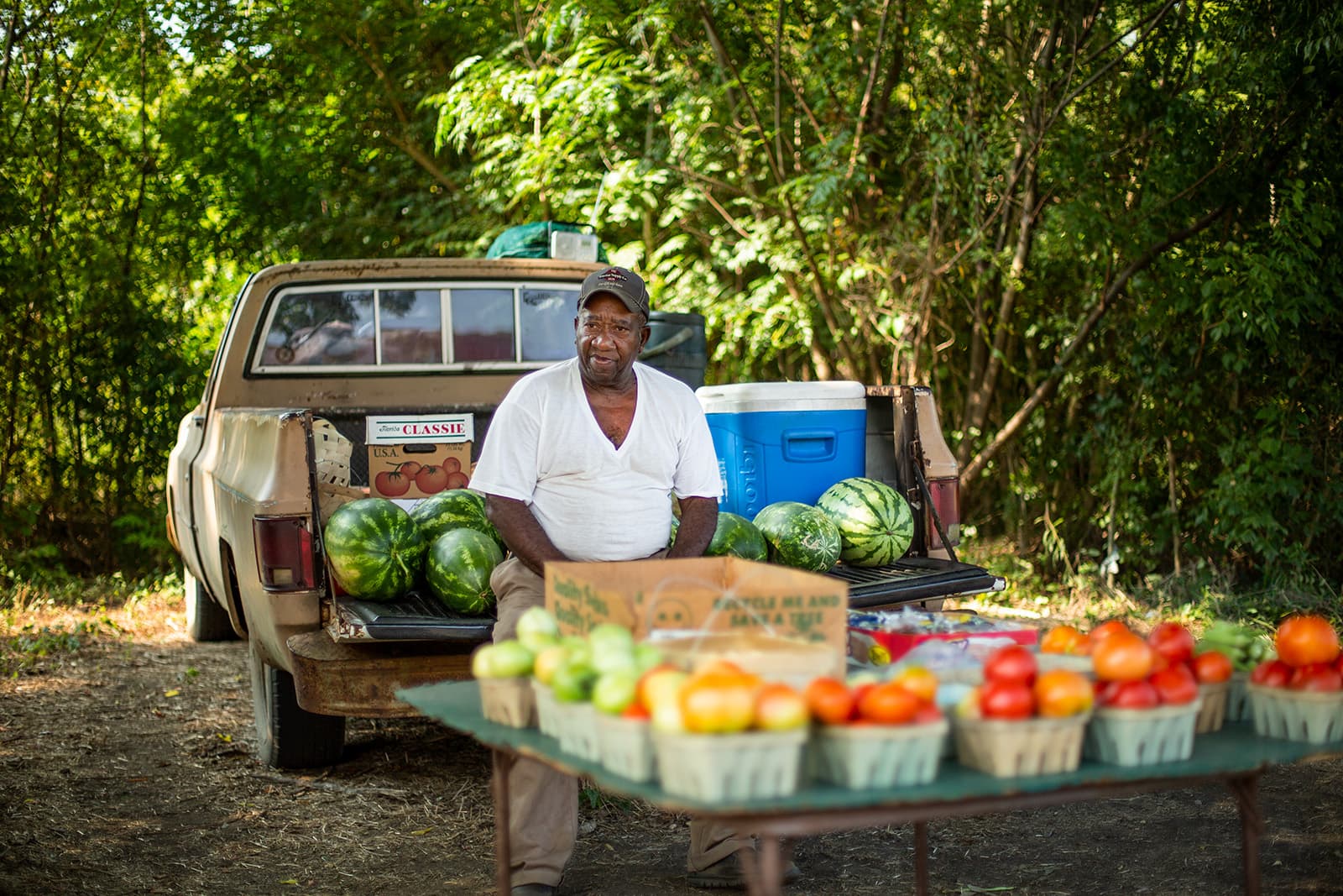 Man sits in front of a table full of produce. 
