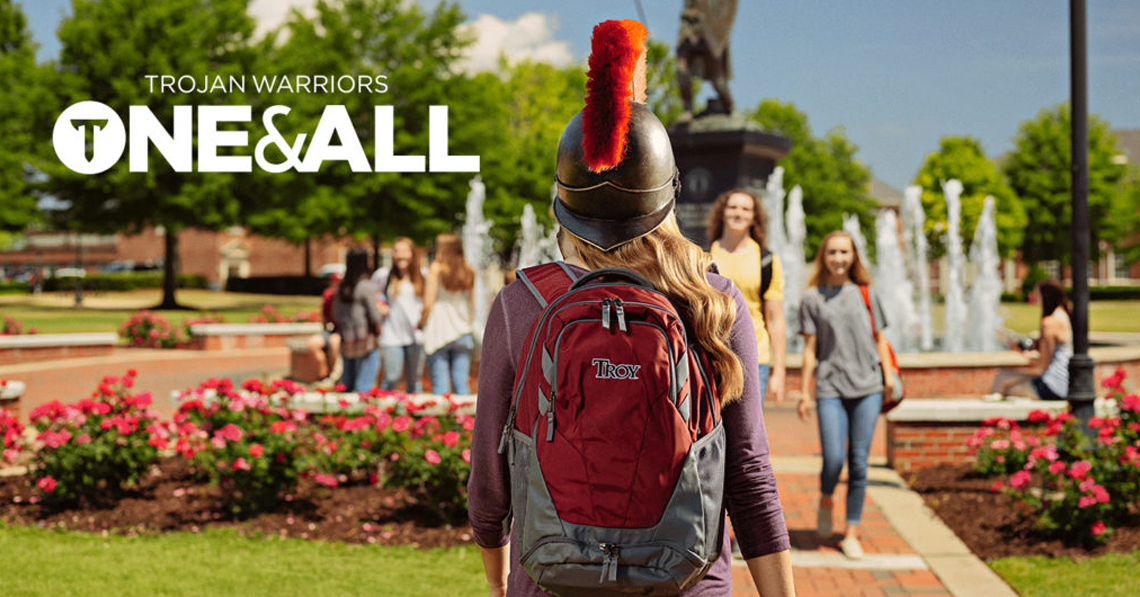Trojan Warriors One & All, TROY student in helmet walking toward a fountain on the quad of the Troy, Alabama campus