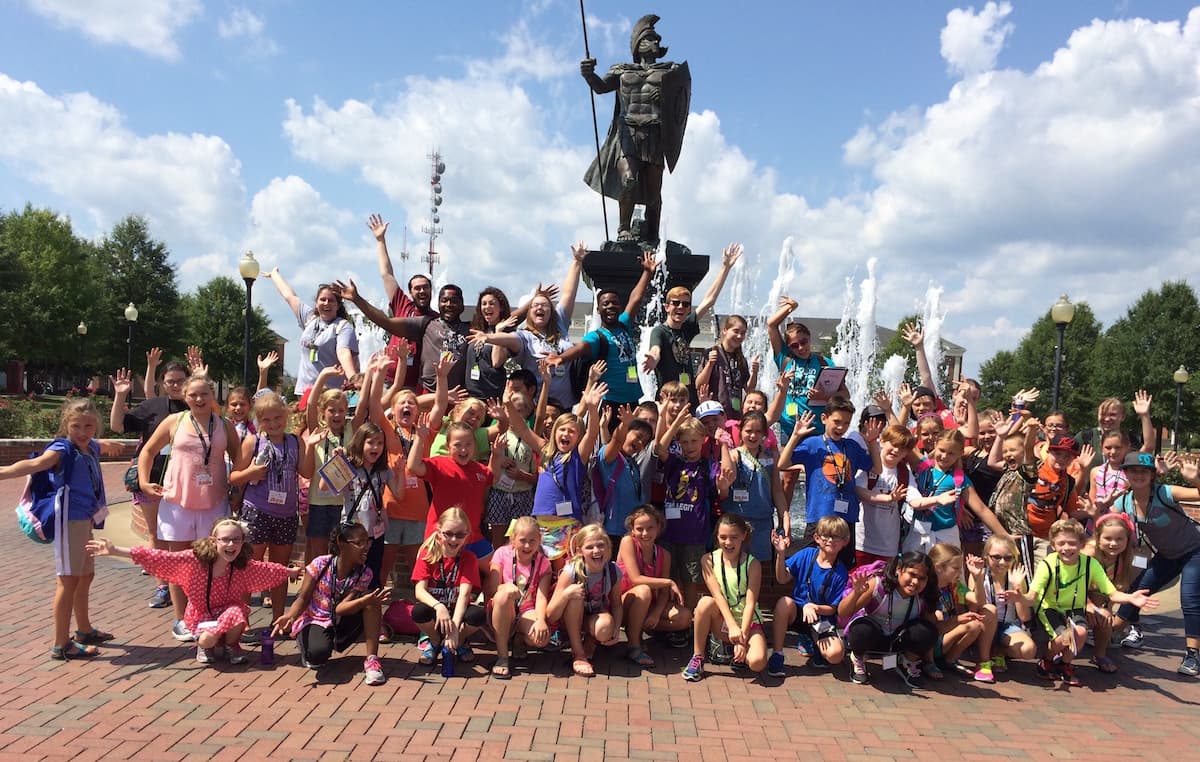 A group of young people pose around the Trojan fountain on the quad