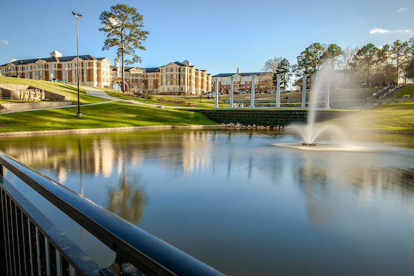 Troy University lake with a water fountain and bridge features and Rushing Hall in the background