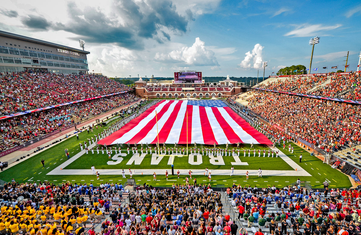 Large American flag spread across football field by marching band