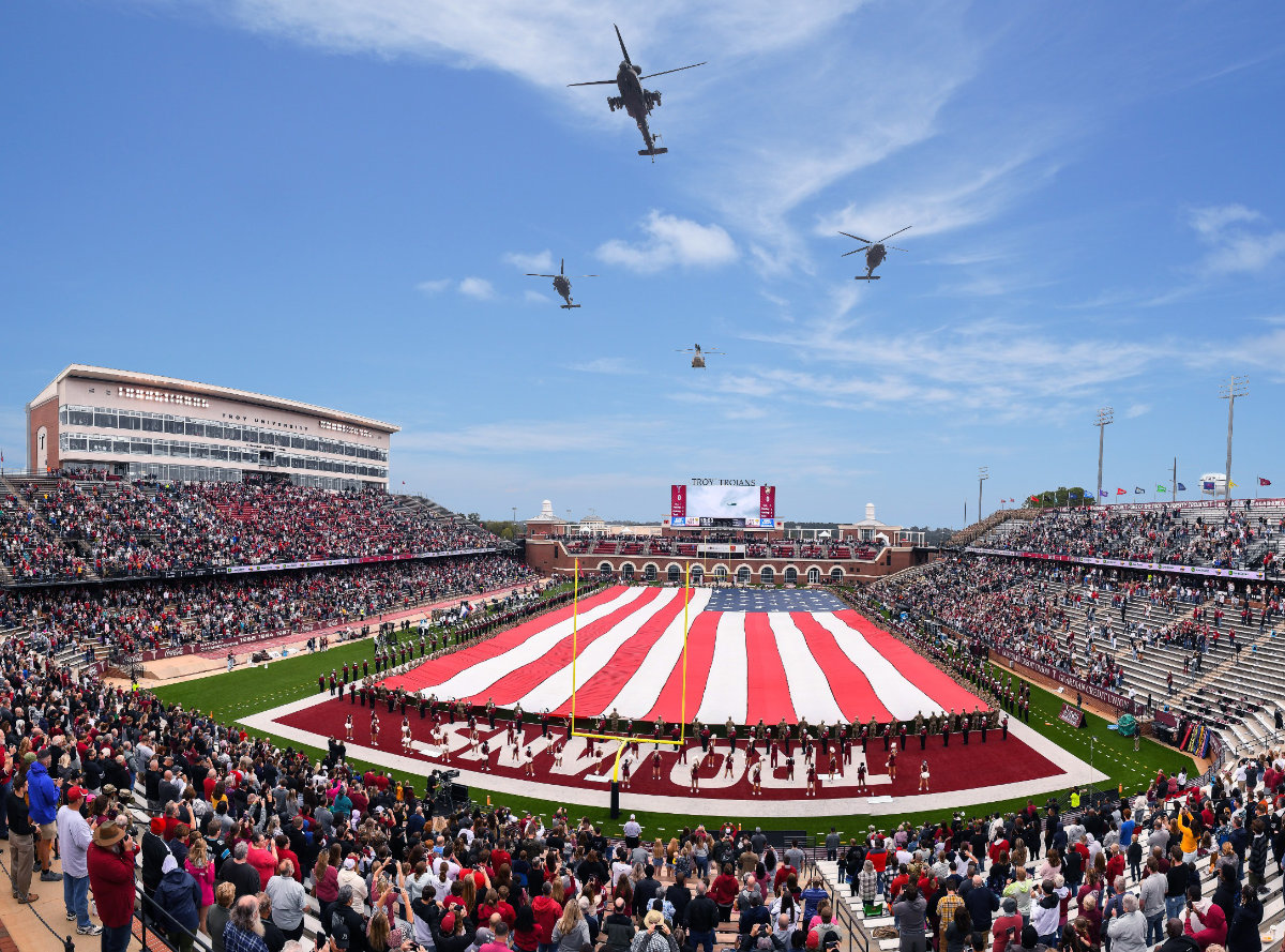 American flag covering Troy Trojans football field with military helecopters overhead